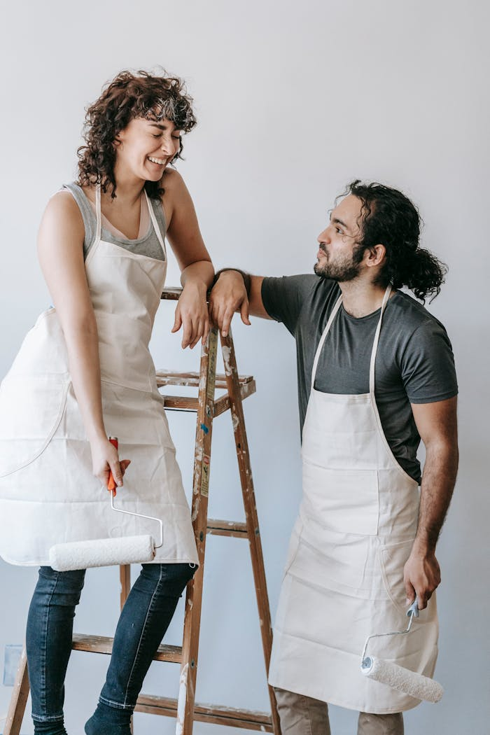 A young couple happily renovating their home with paint rollers and ladders.